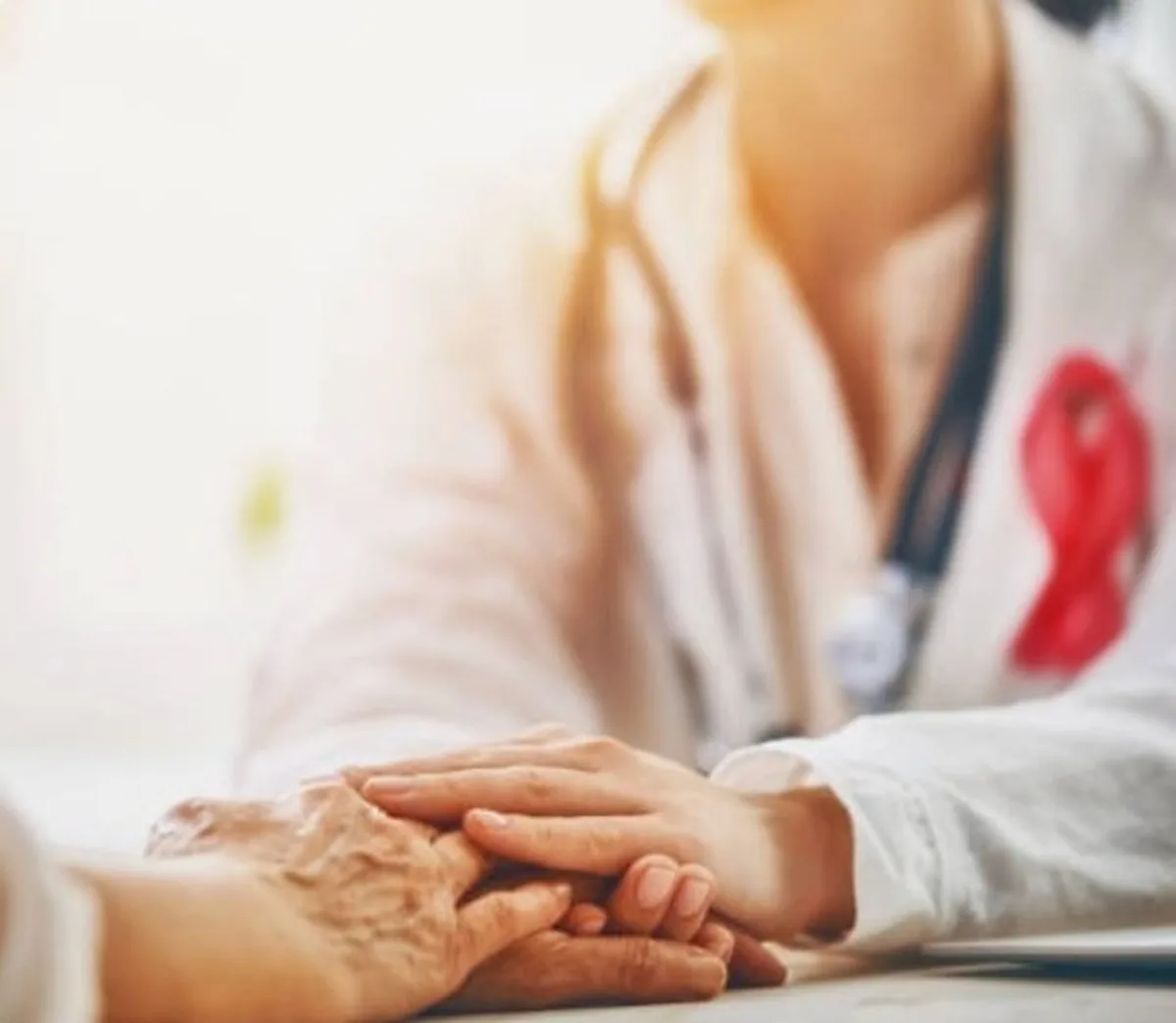 Doctor holding a patient’s hands in reassurance, with a cancer awareness ribbon on her coat